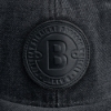 Close-up of the front patch of the hat. It’s a black circular patch on top of the black denim. The patch has a B written on it.