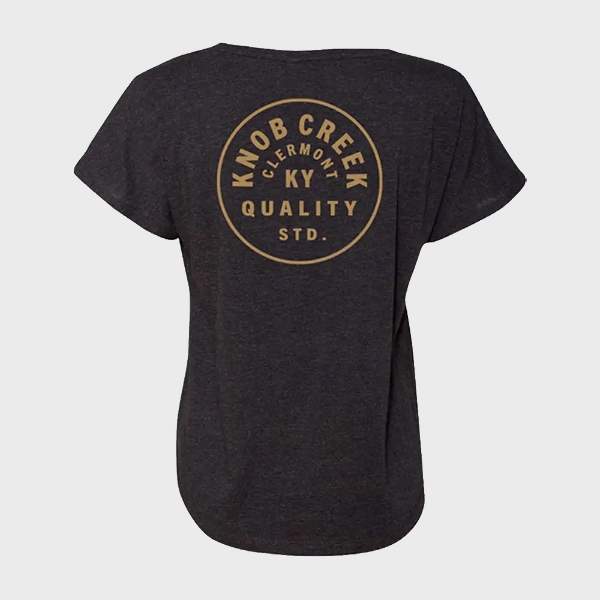 A black woman’s t-shirt viewed from the back, with a golden circle written “Knob Creek, Clermont, KY” inside.