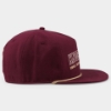 Side view of the burgundy Knob Creek canvas cap showing its structured crown, flat visor, embroidered eyelets, and gold rope accent.